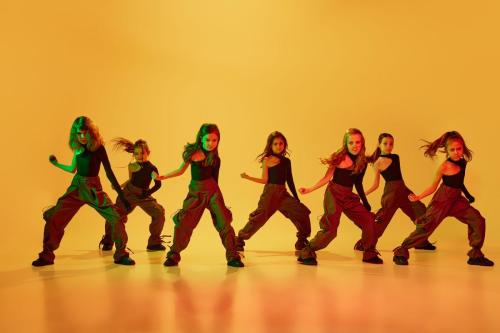 Coordinated movements. Group of little talented girls, children in sport style clothes dancing hip-hop against yellow studio background in neon light